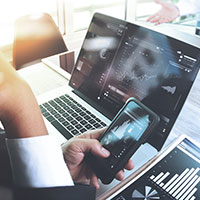 business-person-looking-at-phone-next-to-computer-with-graphs