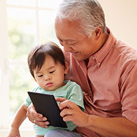 grandfather-holding-infant-and-looking-at-tablet-smiling