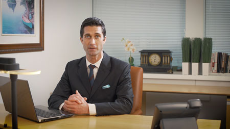 man-in-dark-suit-and-dark-tie-looking-at-camera-next-to-computer