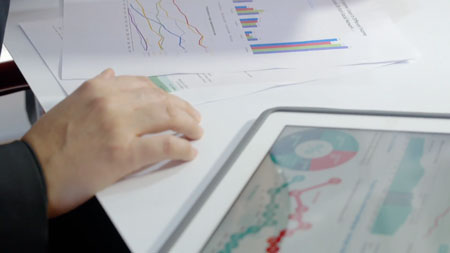 hand-on-stack-of-papers-next-to-tablet-with-graphs